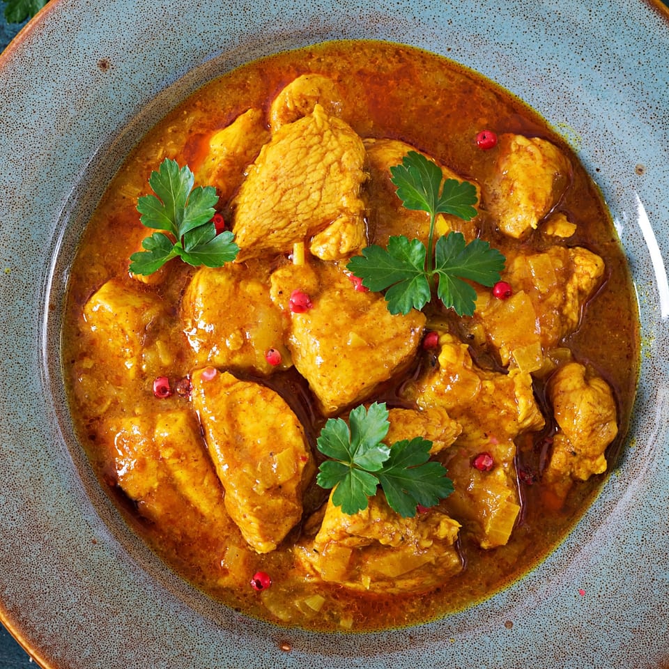 Clayoven Indian Cuisine's chicken curry, garnished with fresh parsley and red peppercorns in a blue bowl.