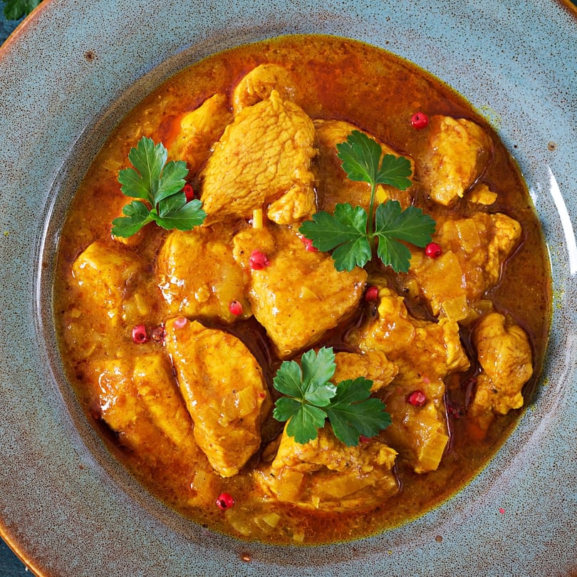 Clayoven Indian Cuisine's chicken curry, garnished with fresh parsley and red peppercorns in a blue bowl.