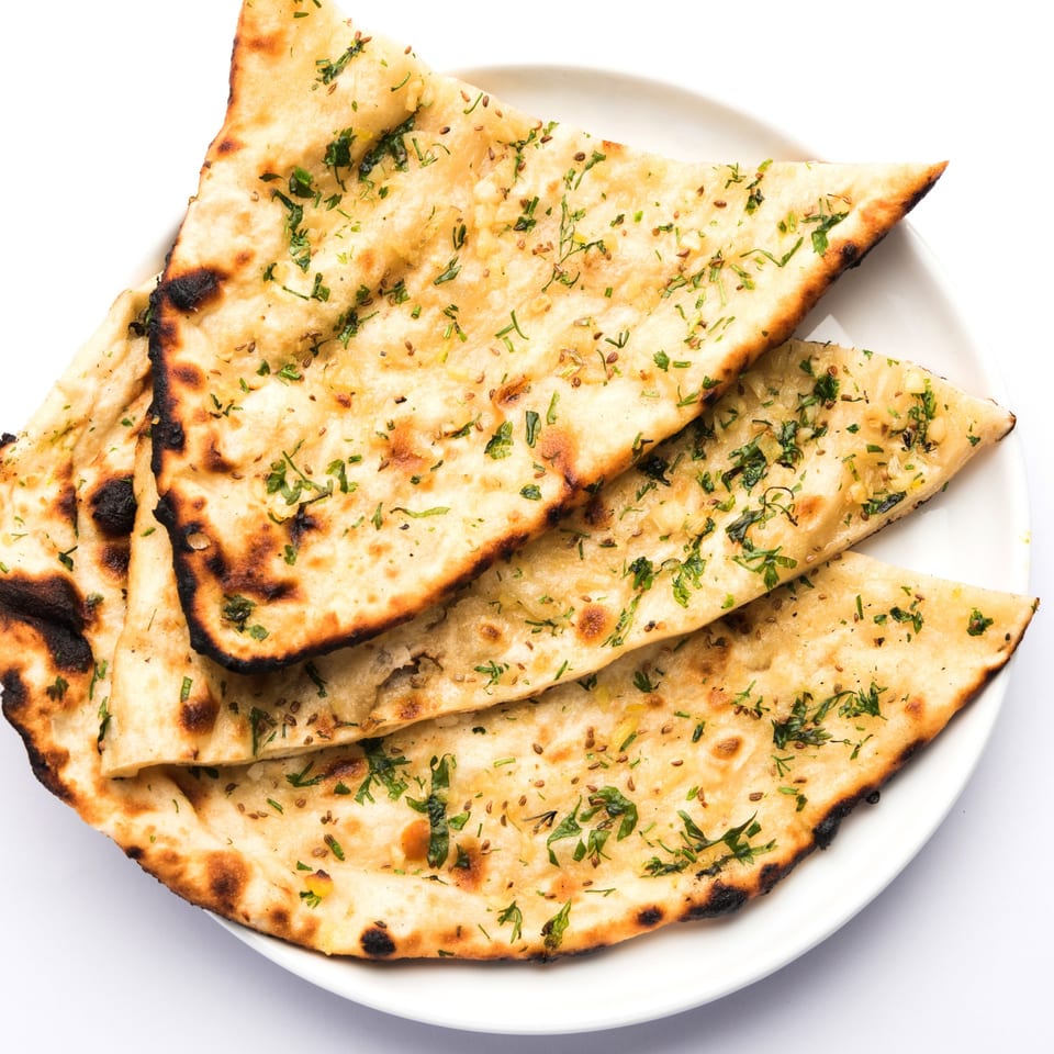 Golden brown garlic naan bread, garnished with fresh herbs and spices, on a white plate.