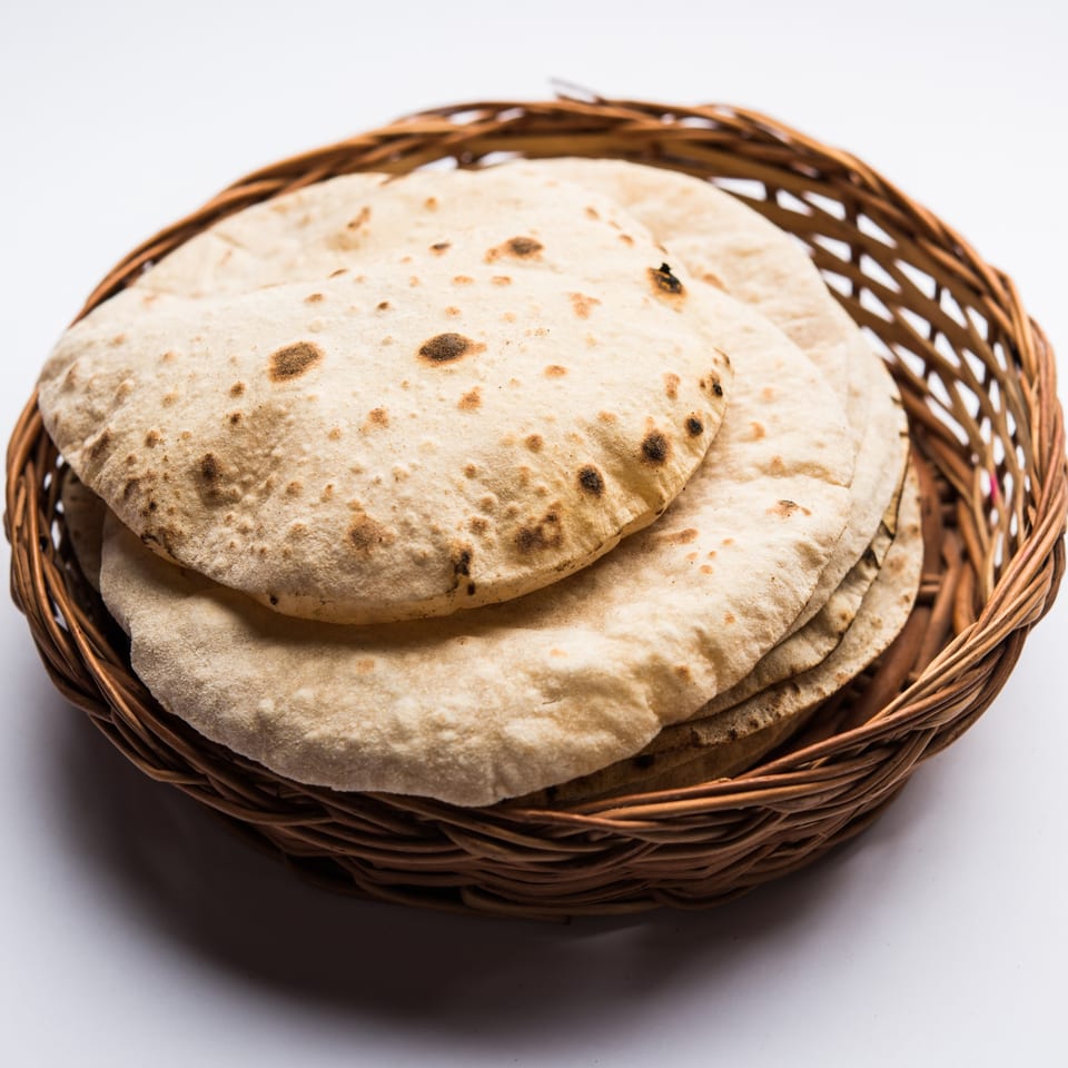 A woven basket filled with several round, lightly browned Indian flatbreads, likely rotis or chapatis.